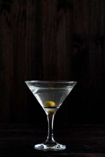 cóctel de margarita en el bar. copa de martini de cóctel con aceitunas sobre fondo de madera. Gafas para martini en la mesa negra. espacio de copia. bebidas alcohólicas. vertical - Foto, Imagen