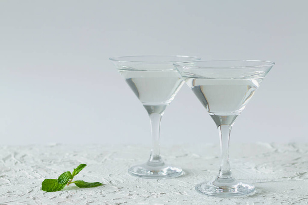 δύο ποτήρια μαρτίνι κοκτέιλ με πράσινη μέντα σε λευκό φόντο. αλκοολούχα ποτά. Ποτήρια για κοκτέιλ στο τραπέζι. αντίγραφο χώρου - Φωτογραφία, εικόνα