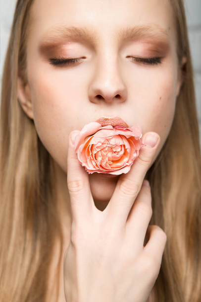 Portret van een mooie jonge vrouw met een rozenbloem in haar mond. Schoonheid en mode. - Foto, afbeelding