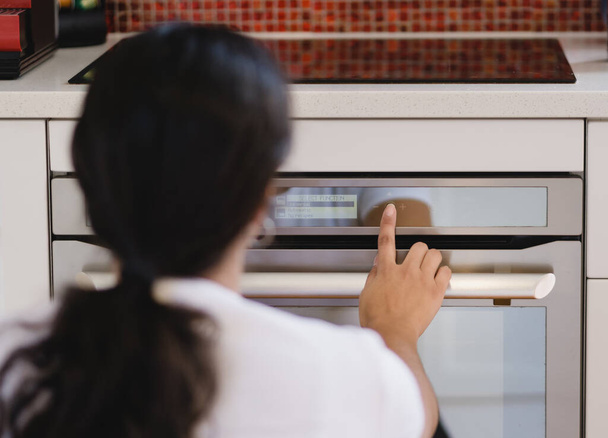 Γυναίκα αφής οθόνη στο σύγχρονο φούρνο για να μαγειρέψουν. Τεχνολογική έννοια. - Φωτογραφία, εικόνα