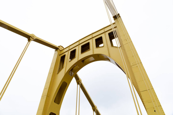 Amarelo ereto de uma ponte suspensa auto-ancorada visto de baixo, céu branco, aspecto horizontal - Foto, Imagem
