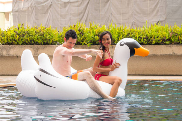 Asyalı Taylandlı kız, beyaz adamla seksi iç çamaşırlı, kırmızı bikinili kadın yüzme havuzunda kuğu balonunda oturuyor.. - Fotoğraf, Görsel