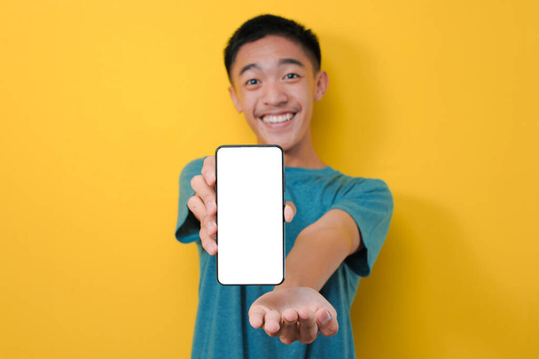 Happy innoissaan nuori aasialainen mies shokki osoittaa valkoinen puhelin näytön kamera, eristetty keltaisella taustalla - Valokuva, kuva