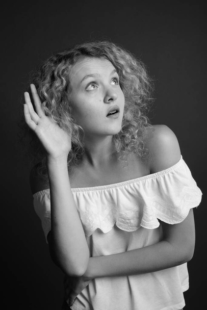 Στούντιο πλάνο της νεαρής όμορφης γυναίκας με ξανθά σγουρά μαλλιά σε γκρι φόντο - Φωτογραφία, εικόνα