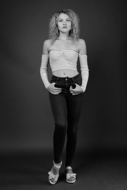 Studio shot of young beautiful woman with blond curly hair against gray background - Photo, image