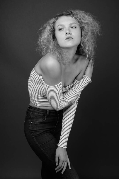 Studio shot of young beautiful woman with blond curly hair against gray background - Foto, immagini
