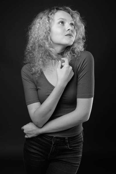 Studio shot van jonge mooie vrouw met blond krullend haar tegen grijze achtergrond - Foto, afbeelding
