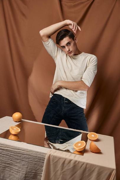 A handsome man sits at a table in front of a mirror with oranges - Photo, Image