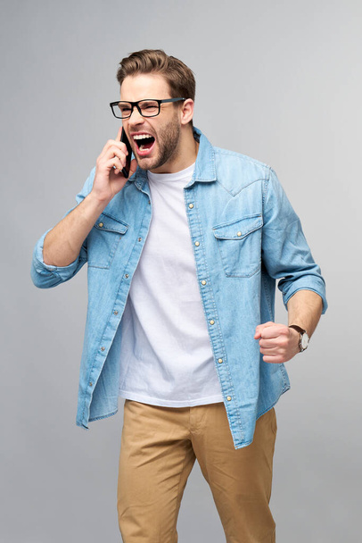 pretty casual man in blue jeans shirt holding his phone standing over studio grey background - 写真・画像