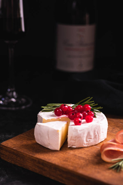 Camembert cheese decorated with red currant on a wooden board and red wine - Фото, зображення