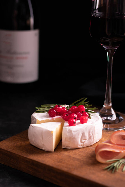 Camembert cheese decorated with red currant on a wooden board and red wine - Zdjęcie, obraz