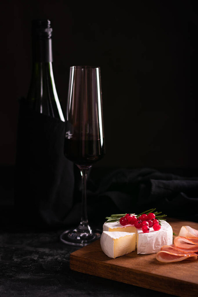 Queijo Camembert decorado com groselha vermelha em uma tábua de madeira e vinho tinto - Foto, Imagem