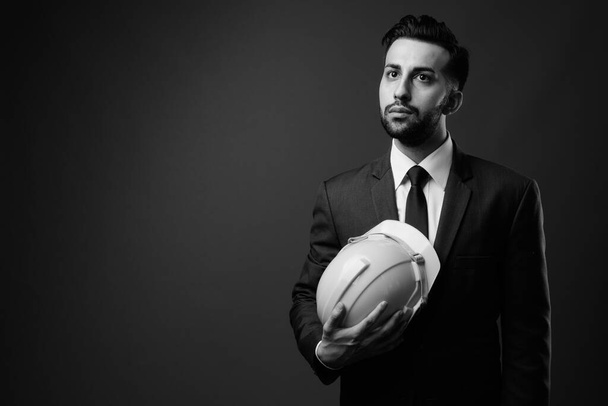 Studio shot of young handsome bearded Iranian businessman with hardhat against brown background - Φωτογραφία, εικόνα