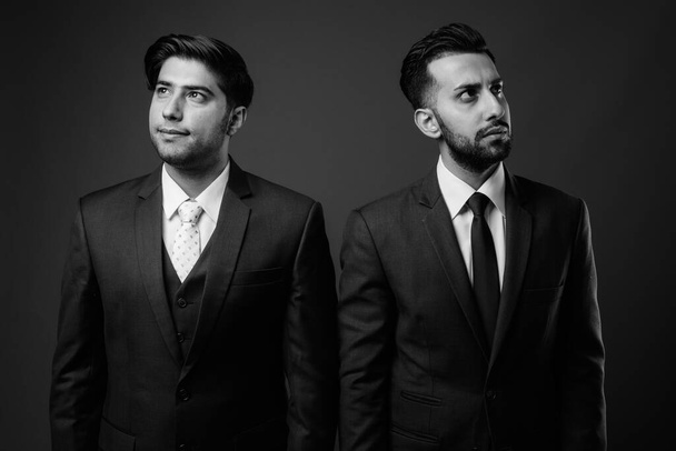 Studio shot of two young Iranian businessmen together against brown background - Photo, Image
