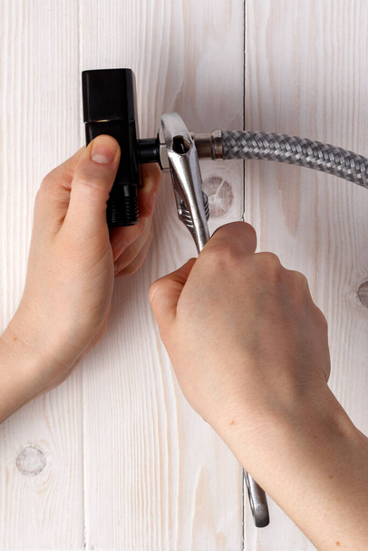 Female plumber connecting flexible hose to black water stopcock. On white wooden background. - Фото, зображення