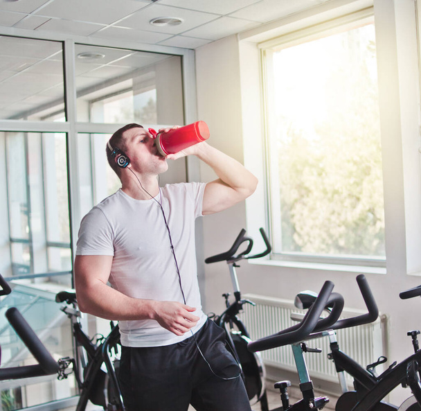 Man drinking water and listening music on exercise bike at spinning class - Photo, Image