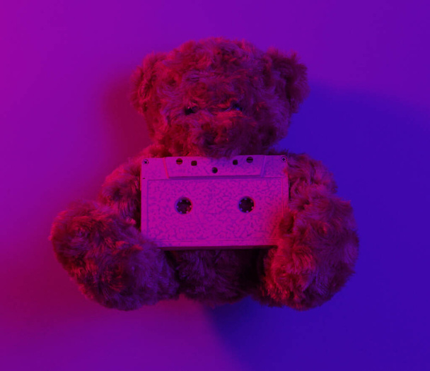 Musikliebhaber Konzept Teddybär halten Audio-Kassette in rot-blauem Neonlicht. Ansicht von oben. 80er Jahre im Retro-Stil. Minimalismus - Foto, Bild