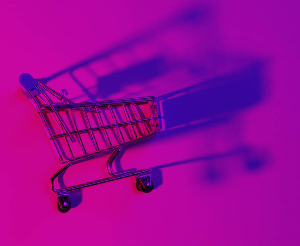 Spielzeug-Einkaufswagen mit neonrosa blauem Licht. Retro 80er Jahre, Minimalismus - Foto, Bild