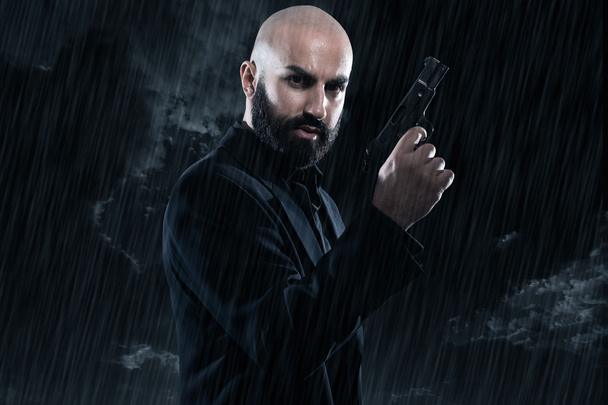 Peligroso hombre gángster calvo con barba sosteniendo arma. Usando blac
 - Foto, Imagen