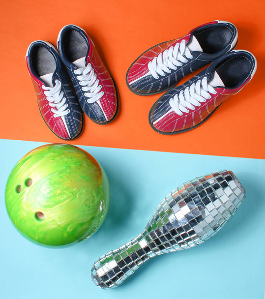 Bowling-Schuhe, Disco-Spiegel-Kegel und Bowlingball auf blau-orangefarbenem Hintergrund. Indoor-Familiensport. Ansicht von oben. Minimalismus - Foto, Bild