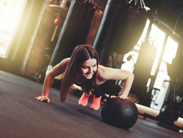 Vrouw doet push-ups met medicijnbal in donkere sportschool - Foto, afbeelding