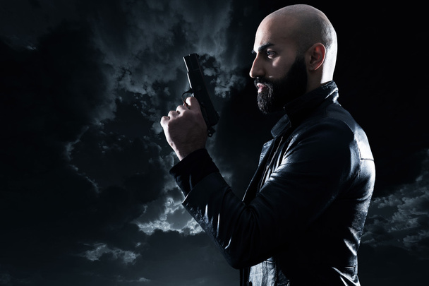 Dangerous bald gangster man with beard holding gun. Wearing blac - Fotografie, Obrázek