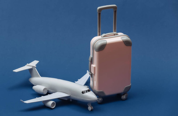 航空旅行の概念。ミニプラスチック旅行スーツケースと古典的な青の背景の航空機. - 写真・画像