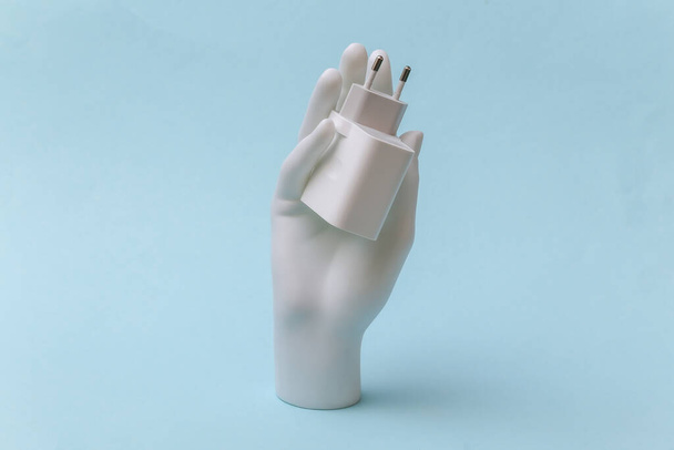 Bílá figurína ruka držení nabíječka adaptér na modrém pozadí - Fotografie, Obrázek