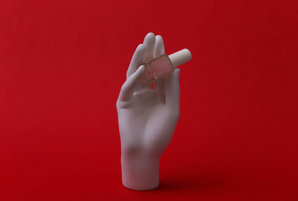 White mannequin hand holding nailpolish bottle on red background. Beauty and fashion concept - Foto, immagini