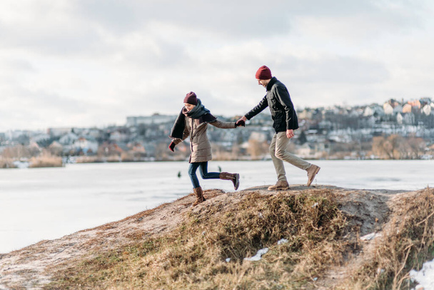 Cool valentine. Happy loving couple walking in snowy winter lake, spending Christmas vacation together. Outdoor seasonal activities. Lifestyle capture. - 写真・画像