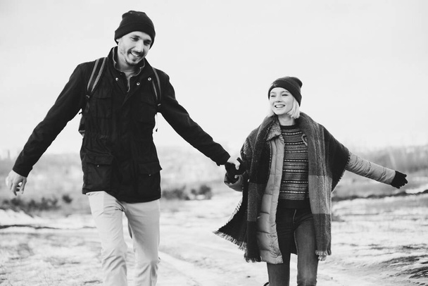 Black and white. Cool valentine. Happy loving couple walking in snowy winter field, spending Christmas vacation together. Outdoor seasonal activities. Lifestyle capture. - Foto, imagen