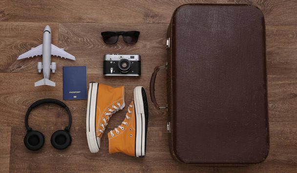 Travel concept. Retro style sneakers and old travel suitcase, accessories on wooden floor. Top view - Photo, Image