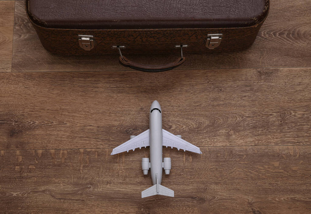 Travel concept. Air plane and old travel suitcase on wooden floor. Top view - Photo, Image