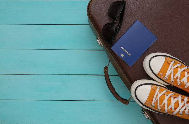 旅行のコンセプト。レトロスタイルのスニーカーや古い旅行スーツケース、青い木製の背景のアクセサリー。トップ表示 - 写真・画像