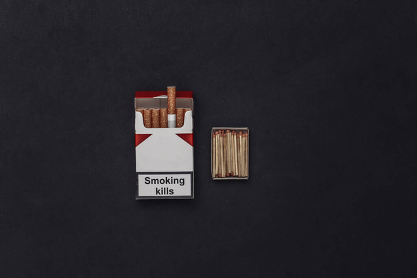 Paquete de cigarrillos y fósforos sobre un fondo negro. Vista superior - Foto, Imagen