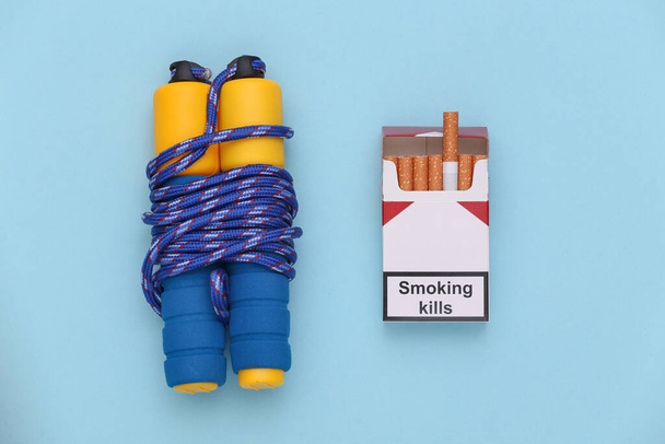 Esporte ou conceito de maus hábitos. Salte corda e um maço de cigarros no fundo azul. Vista superior - Foto, Imagem