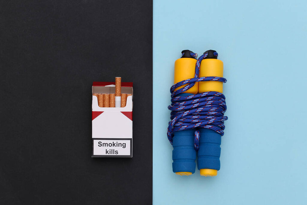 Sport or bad habits concept. Jump rope and a pack of cigarettes on blue black background. Top view - Photo, Image