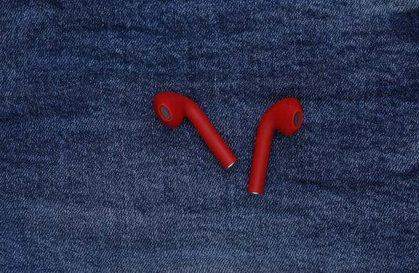 Красные беспроводные наушники с футляром зарядки на фоне синих джинсов - Фото, изображение