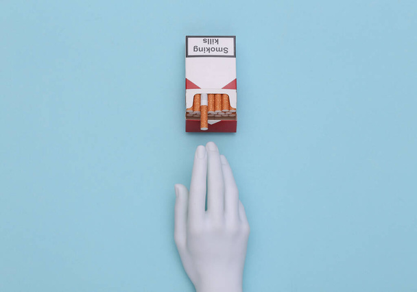 Manichino mano contenente pacchetto di sigarette su sfondo blu - Foto, immagini