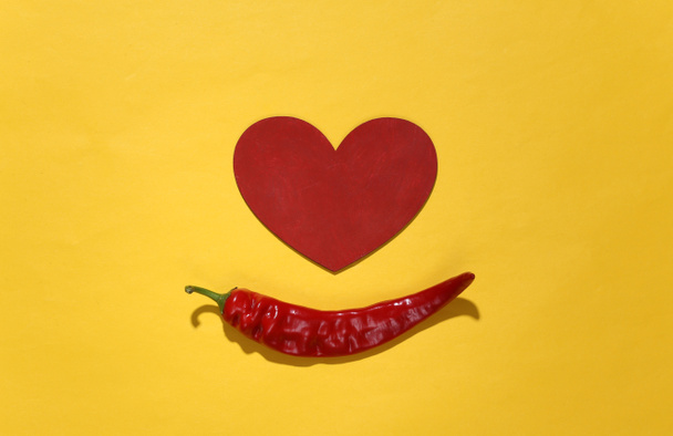Chili pippuri ja sydän keltaisella pohjalla. Rakkauden käsite. Yläkuva - Valokuva, kuva
