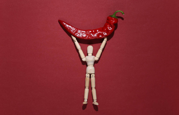 Деревянная кукла держит красный перец чили на красном фоне - Фото, изображение