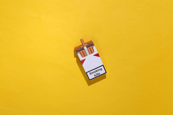 Envase de cigarrillos sobre fondo amarillo brillante. Fumar mata. Vista superior - Foto, Imagen