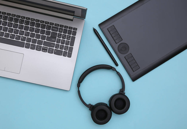 Laptop und Grafik-Tablet mit Stift, Kopfhörer auf blauem Hintergrund. Ansicht von oben. Flache Lage - Foto, Bild