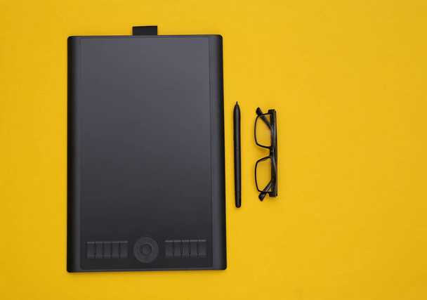 Graphic tablet with pen and glasses on yellow background. Top view - Photo, Image