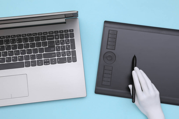 La main de Menequin fonctionne sur une tablette graphique et un ordinateur portable. Fond bleu - Photo, image