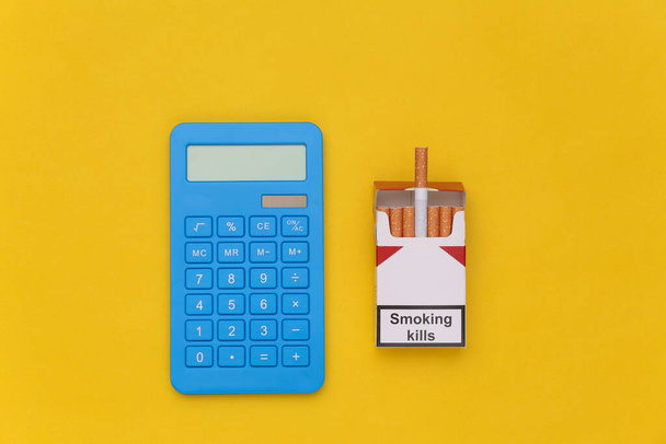 Pakkaus savukkeita ja laskin keltaisella pohjalla. Tupakoinnin kustannukset - Valokuva, kuva