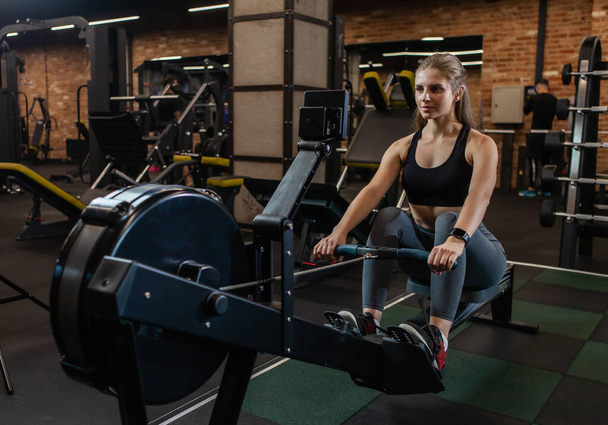 Αθλητική γυναίκα εκπαίδευση στη μηχανή κωπηλασίας στο γυμναστήριο - Φωτογραφία, εικόνα
