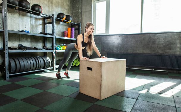 Beautiful slim young sports woman doing push ups on fitness box at gym - Photo, image