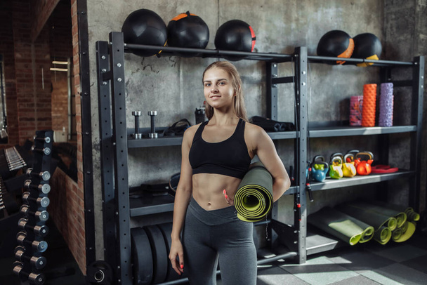 Fit woman with perfect body holds rolled mat in the gym and and posing on the camera - Photo, Image