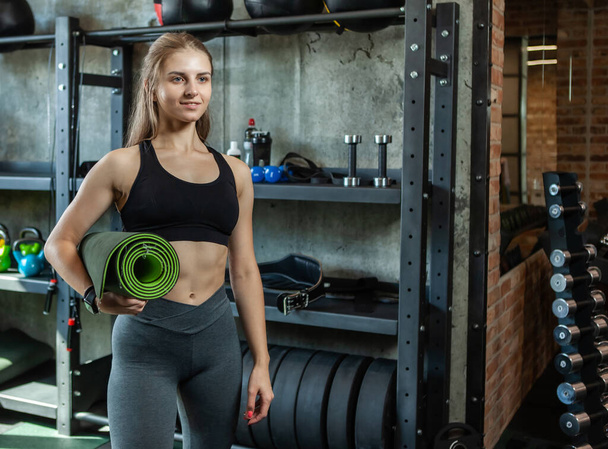 Fit woman with perfect body holds rolled mat in the gym and and posing on the camera - Photo, Image